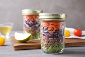 Glass jars with healthy meal on light grey wooden table