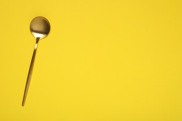 One shiny golden spoon on yellow background, top view. Space for text