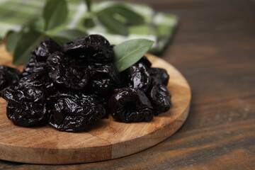 Tasty dried prunes and green leaf on wooden table, closeup