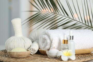 Composition with different spa products and plumeria flower on wicker mat indoors