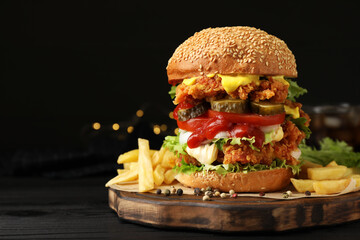 Delicious burger with crispy chicken patty and french fries on black wooden table. Space for text