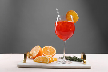 Glass of tasty Aperol spritz cocktail with orange slices and rosemary on white table against gray background, space for text