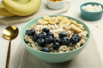 Tasty oatmeal with banana, blueberries, coconut flakes and honey served in bowl on beige table