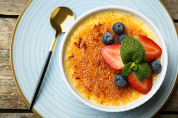 Delicious creme brulee with berries and mint in bowl on wooden table, top view