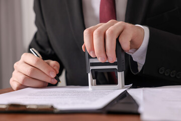 Notary with pen stamping document at table in office, closeup