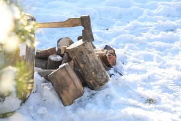 Metal axe in wooden log and pile of wood outdoors on sunny winter day. Space for text