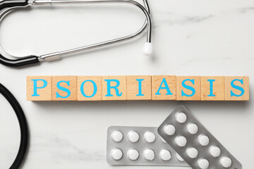 Word Psoriasis made of wooden cubes with letters, stethoscope and pills on white marble table, flat...