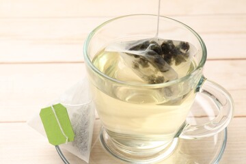Putting tea bag in glass cup on light wooden table, closeup