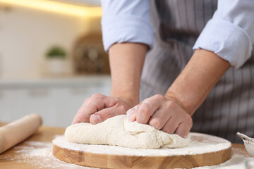 Making bread. Man kneading dough at wooden table in kitchen, closeup