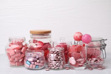Tasty pink candies in glass jars on white background