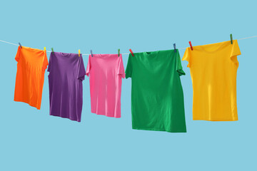 Colorful t-shirts drying on washing line against light blue background