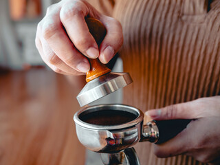 Close-up of hand Barista cafe making coffee with manual presses ground coffee using tamper at the coffee shop