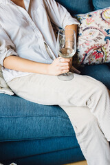 casual elegant woman in white button down shirt and khaki pants holding glass of white wine on blue...