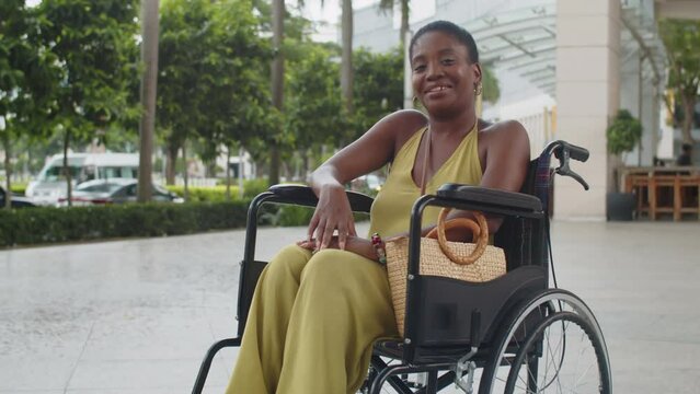 Portrait of cheerful African American woman in yellow jumpsuit with disability smiling at camera outdoors