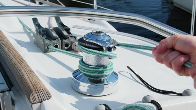 Proficient yachtsman wraps durable nylon cable around winch. Sailor secures lines for safe sailing experience in sea water