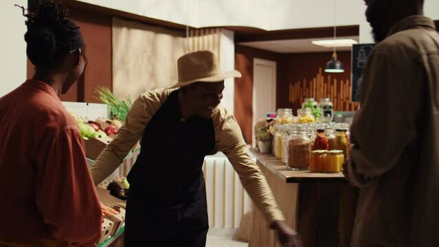 Small business owner opening local supermarket with new goods, greeting regular customers on shopping spree. African american vendor welcoming shoppers at zero waste eco store. Camera B.