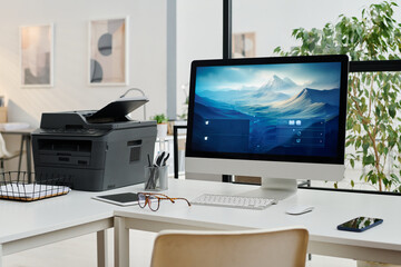 No people shot of modern desktop computer and printer on desk in modern office interior, copy space