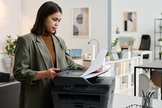 Medium shot of young woman wearing smart casual outfit working in modern office printing documents