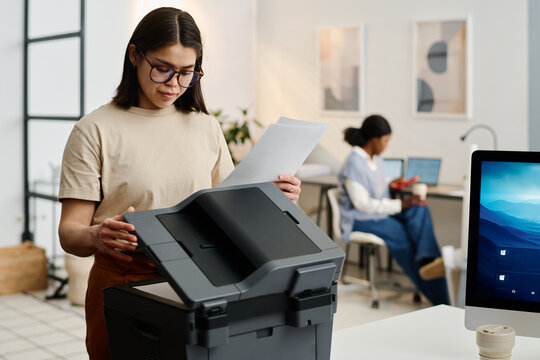 Selective focus shot of young female secretary scanning or making copies of documents in modern office