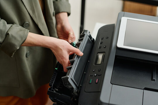 High angle view of unrecognizable female office worker taking ink cartridge out of printer at work in office
