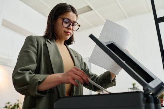 Low angle view of young woman wearing eyeglasses working in office making copies of documents