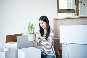 引越しの段ボールに囲まれて植物の鉢を持っている女性