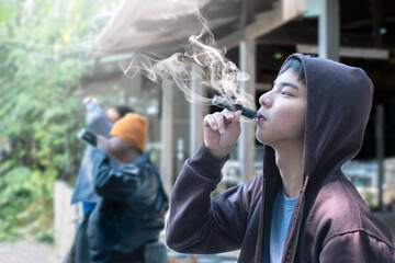 Asian male teenager is smoking electronic cigarette or vapor and drinking alcohol with friends in secret area, soft focus, daily life problems and bad habit and behavior of teenagers concept. - obrazy, fototapety, plakaty