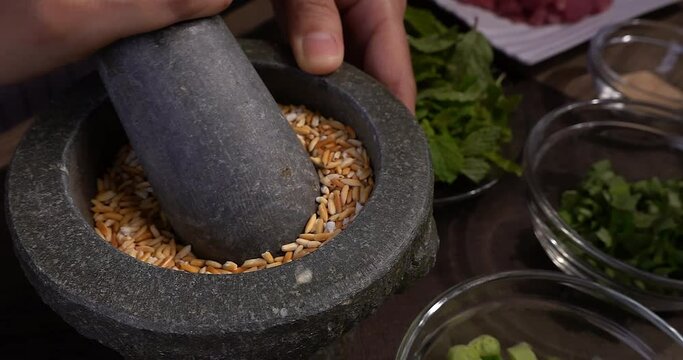 Original name(s): Close up view of Slow Motion of Grinding roasted rice in a stone mortar in Thai style, preparing ingredients for cooking Larb menu