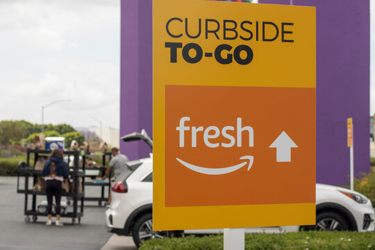 Irvine, CA, USA - May 8, 2022: Closeup of the Curbside To-Go sign in a parking lot outside an Amazon Fresh grocery store in Irvine, California. Customers are seen loading their cars with pickup bags.
