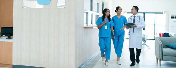 Mature female doctor discussing medical report with nurses in hospital hallway. Senior general...