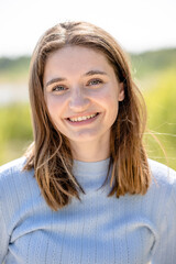 Fototapeta premium The photograph is a sunlit portrait of a young woman with a bright and friendly smile. The setting appears to be outdoors on a sunny day, with natural light casting a soft glow on her face. Her hair