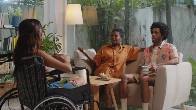 Pan shot of group of diverse friends discussing something while spending time together at home