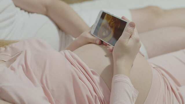 Pregnant woman looks at baby's ultrasound on smartphone, intimate bond through technology. Expectant mother viewing sonogram on phone, modern means of sharing and experiencing joy of new life.
