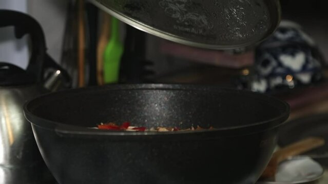 A woman's hand covers a cauldron with food on a gas stove with a lid.
