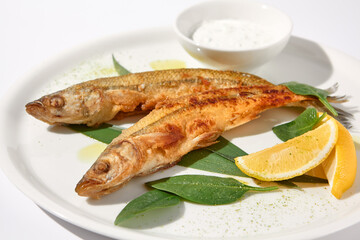 Grilled vendace fish with lemon and sour cream on a white plate, ideal for culinary presentations and food marketing