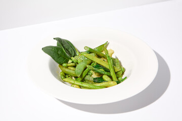 Fresh green vegetable garnish featuring asparagus, zucchini, and edamame beans on isolated white background