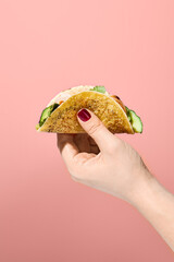 Woman's hand holding a corn tortilla taco filled with sweet potato mousse and turkey on a pink...