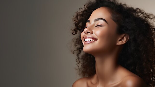 Portrait of beautiful latin woman touching her clean and healthy face against grey background. Smiling hispanic woman with natural makeup feeling healthy skin with eyes closed. Beauty care