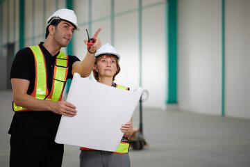 workers or engineers planning from work on blueprint drawing paper and pointing to something in the factory