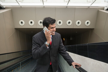 Indian businessman using his Smart phone on an escalator.