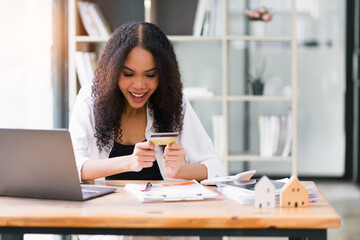 Cheerful young woman shopping online using credit card and laptop at a modern workspace.