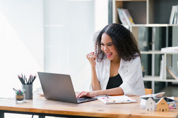 Joyful African American businesswoman cheering while looking at her laptop screen, celebrating a successful moment at work.