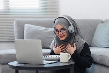 Muslim woman wearing headphones having a delightful online interaction or listening to content on...