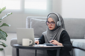 Muslim woman wearing headphones having a delightful online interaction or listening to content on her laptop at home.