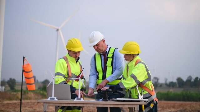 Engineer surveyor and manager wearing uniform walking holding box inspection and tablet work in wind turbine farms rotation to electricity, alternative renewable energy for clean power energy concept.