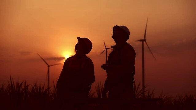 Silhouette engineer surveyor wearing uniform inspection work in wind turbine farms rotation to electricity, alternative renewable energy for clean power energy concept.