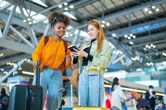 Happy woman friends holding passport and luggage walking together to airline check in counter in airport terminal. Attractive girl enjoy and fun travel on holiday vacation with airplane transportation - Powered by Adobe
