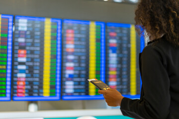 African businesswoman looking flight schedule on timetable and go to check-in and boarding gate in...