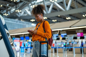 African woman holding passport using self Check-in kiosk machine getting airline ticket boarding...
