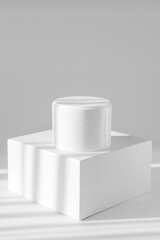 Empty white jar of cream on square stand in sunlight on White isolated background with shadows. 3d podium, Vertical image, close-up
